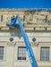 Blue cherry picker lift against a large building with 'State Post' inscription.