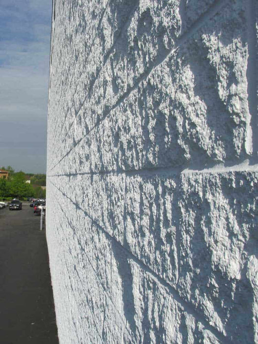 Close-up of a textured stone wall with a blurred street and cars in the background