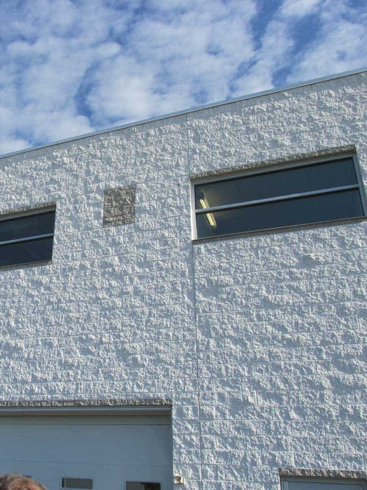 Modern building facade with textured white wall and rectangular windows against a blue sky.
