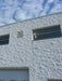Modern building facade with textured white wall and rectangular windows against a blue sky.