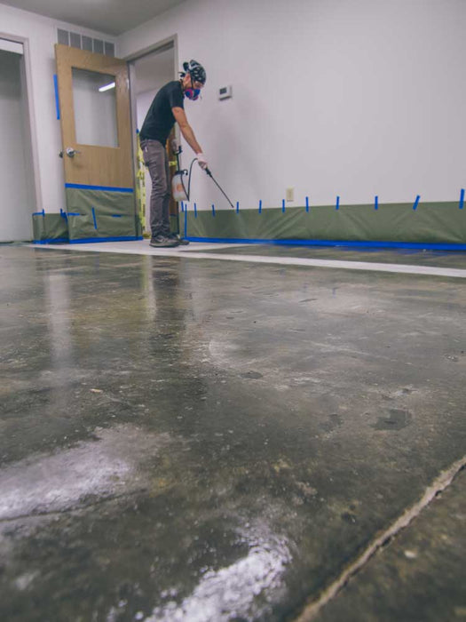 Person applying a floor finish to a concrete floor using a spray gun.
