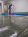 Person applying a floor finish to a concrete floor using a spray gun.