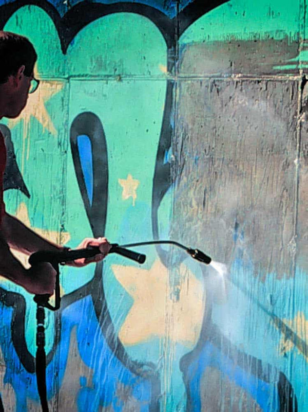 Person using a pressure washer to clean a wall with graffiti
