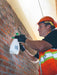 Person in safety gear applying a substance to a brick wall using a spray bottle.