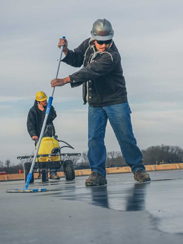 Two workers on a rooftop using tools to prepare a surface for construction.