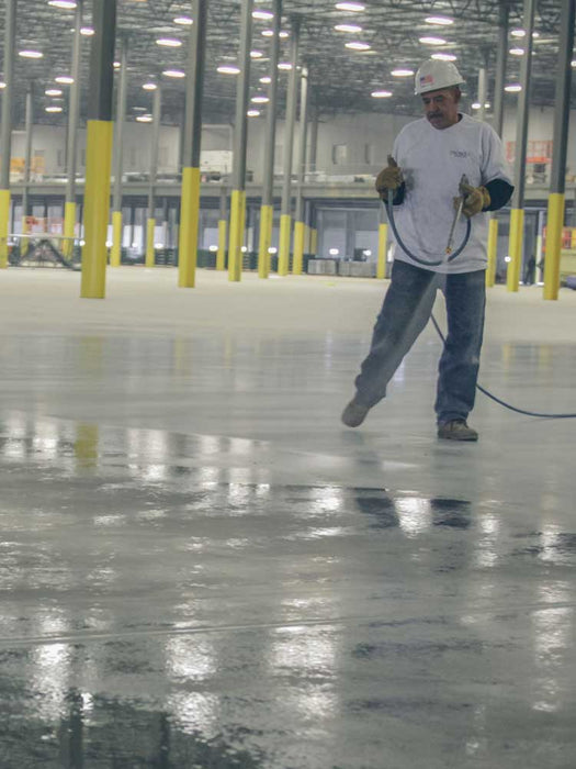 Person cleaning a large industrial floor with a wet mop in a warehouse setting.
