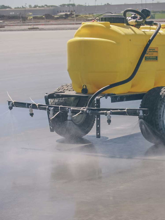 Yellow agricultural sprayer on a field with dust or smoke in the foreground