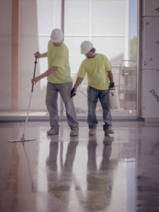 Two workers in yellow shirts and hard hats cleaning a large, shiny floor.