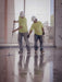 Two workers in yellow shirts and hard hats cleaning a large, shiny floor.