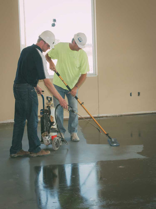 Two workers using floor grinding equipment on a concrete floor.