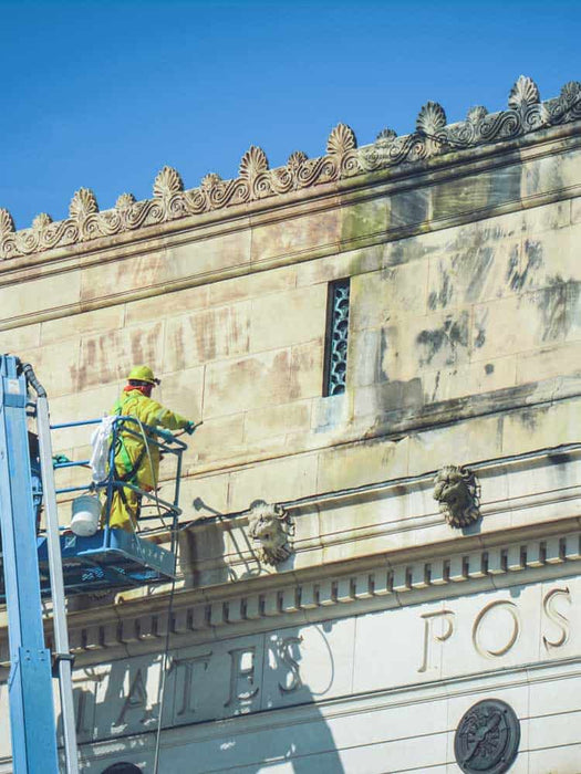 Person on a lift cleaning the exterior of a building with ornate architecture.