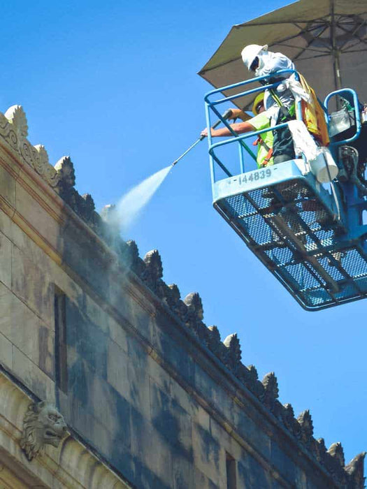 Person on a lift cleaning the top of a building with a blue sky background