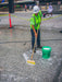 Person cleaning a street with a broom and bucket, with a bus and people in the background.
