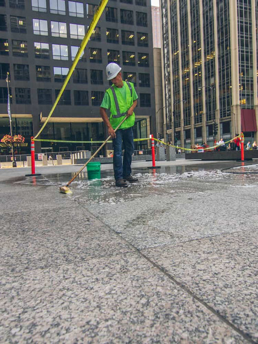 Person cleaning a sidewalk with a street cleaning tool in an urban setting