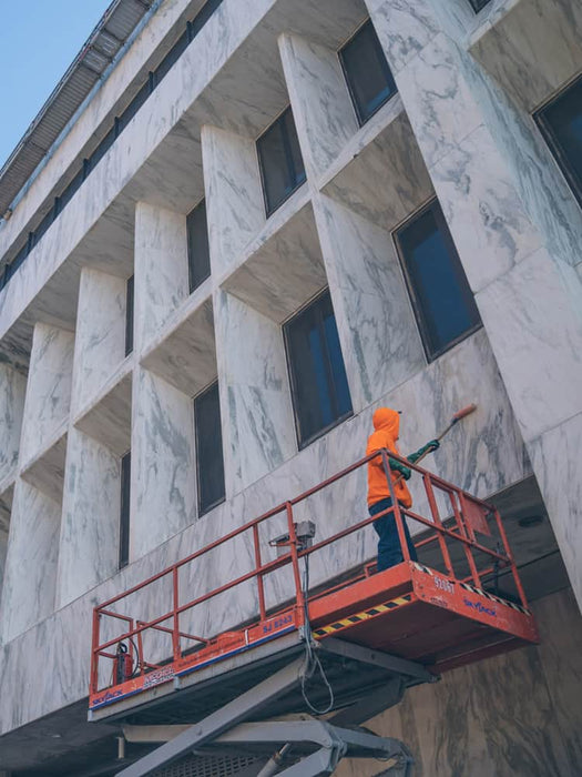 Person on a cherry picker platform cleaning windows of a marble building.
