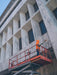 Person on a cherry picker platform cleaning windows of a marble building.