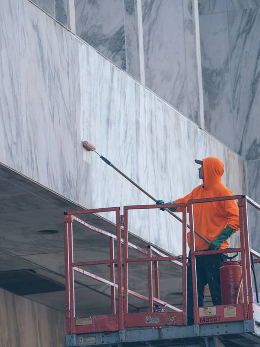Person in orange hoodie cleaning a marble wall with a long-handled tool on a lift.