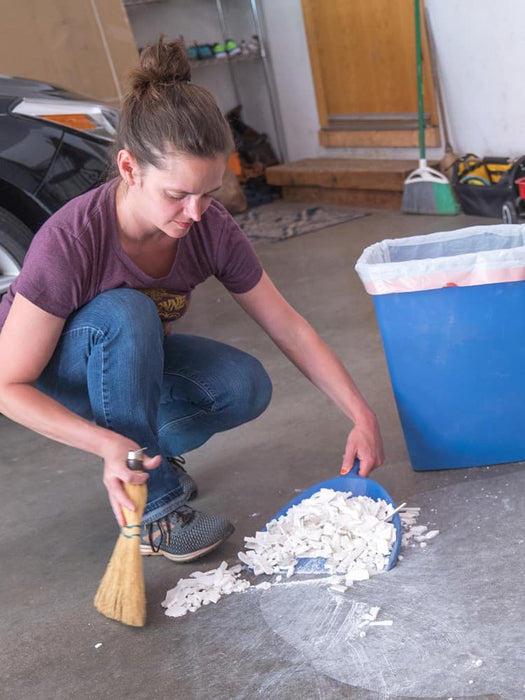 Person cleaning up small items in a garage with a broom and dustpan.
