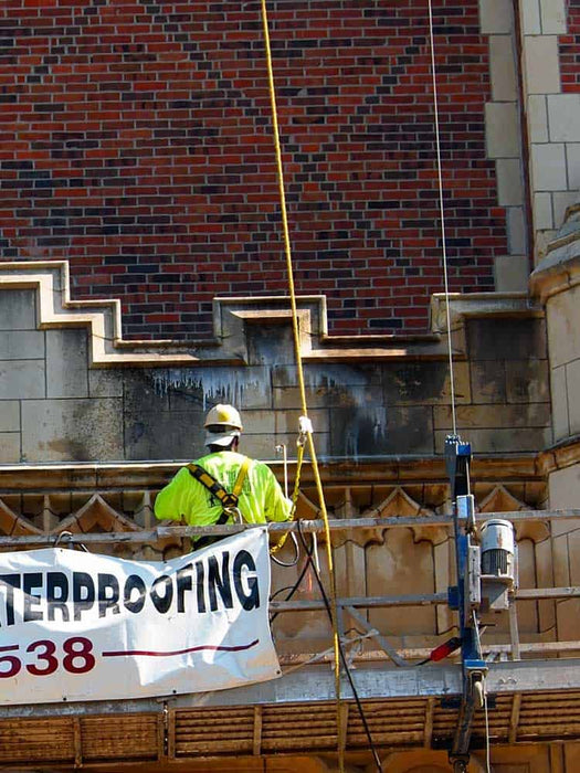Construction worker on a scaffold with waterproofing banner in front of a brick wall.
