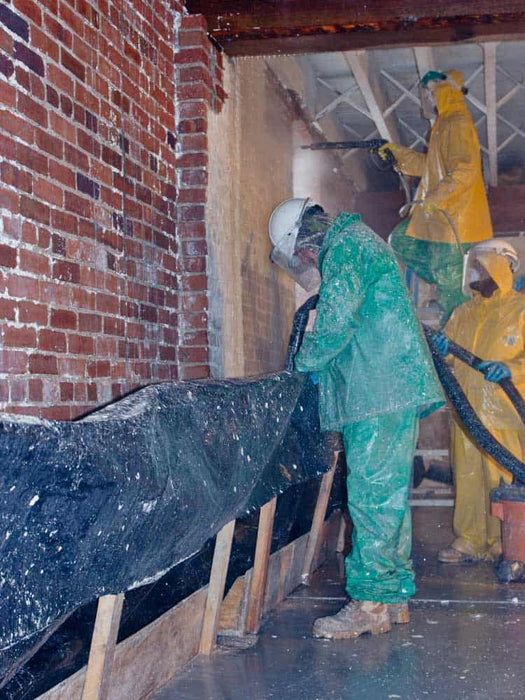 Workers in protective suits applying insulation to a wall.
