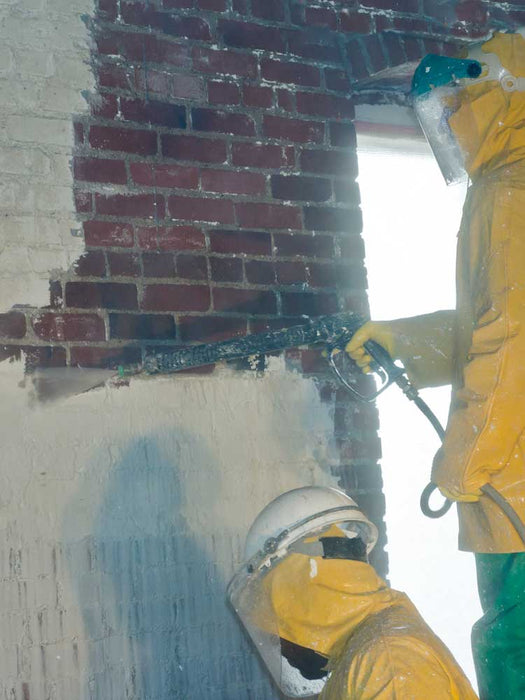 Person in protective gear using a spray gun on a brick wall
