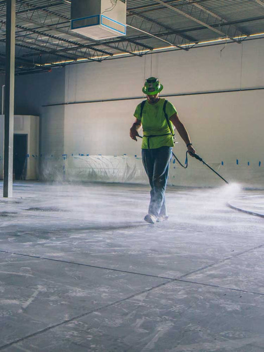 Person in a warehouse using a pressure washer on a concrete floor