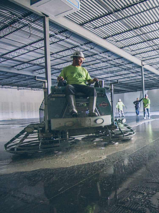Person operating a floor scrubber machine in a large indoor facility.
