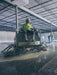 Person operating a floor scrubber machine in a large indoor facility.