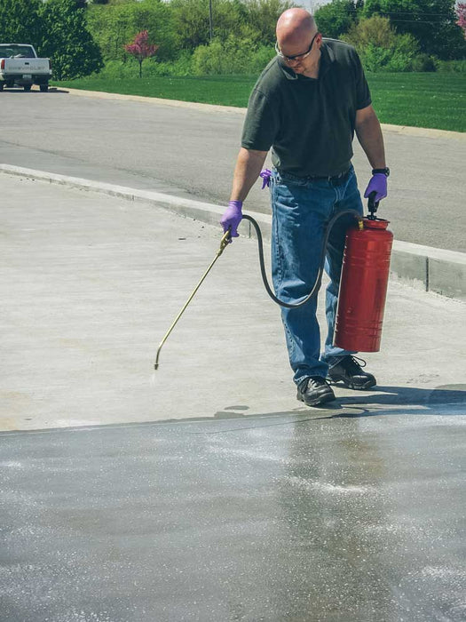 Person using a pressure washer on a driveway with a red fire extinguisher.