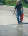 Person using a pressure washer on a driveway with a red fire extinguisher.