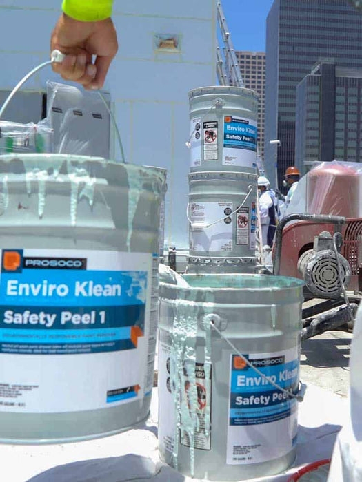Three buckets labeled 'Enviro Klean Safety Peel 1' on a construction site with workers and buildings in the background.