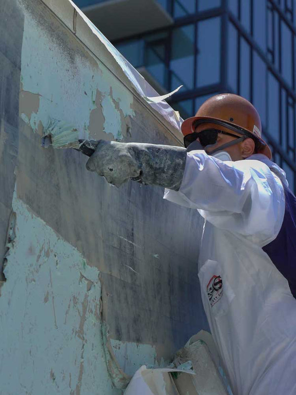 Person in protective gear working on a wall with a tool