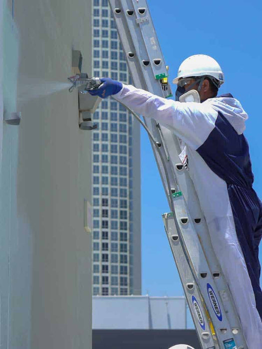 Person on a ladder performing maintenance work on a high-rise building with a clear blue sky.