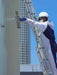 Person on a ladder performing maintenance work on a high-rise building with a clear blue sky.