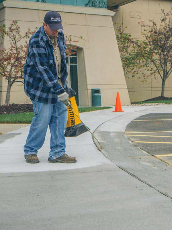 Person working on a sidewalk with safety cones and tools in an outdoor setting