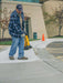 Person working on a sidewalk with safety cones and tools in an outdoor setting