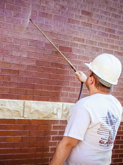 Person applying sealant to a brick wall using a spray gun.