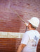 Person applying sealant to a brick wall using a spray gun.