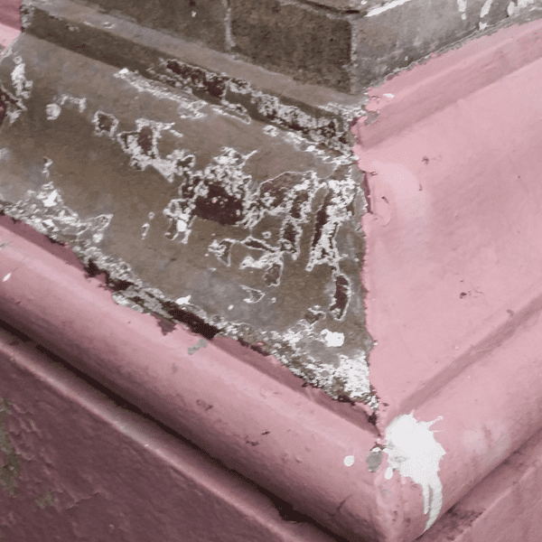 Close-up of a corner where pink and brown materials meet, with peeling paint.