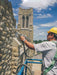 Person using a pressure washer on a stone building with a church tower in the background
